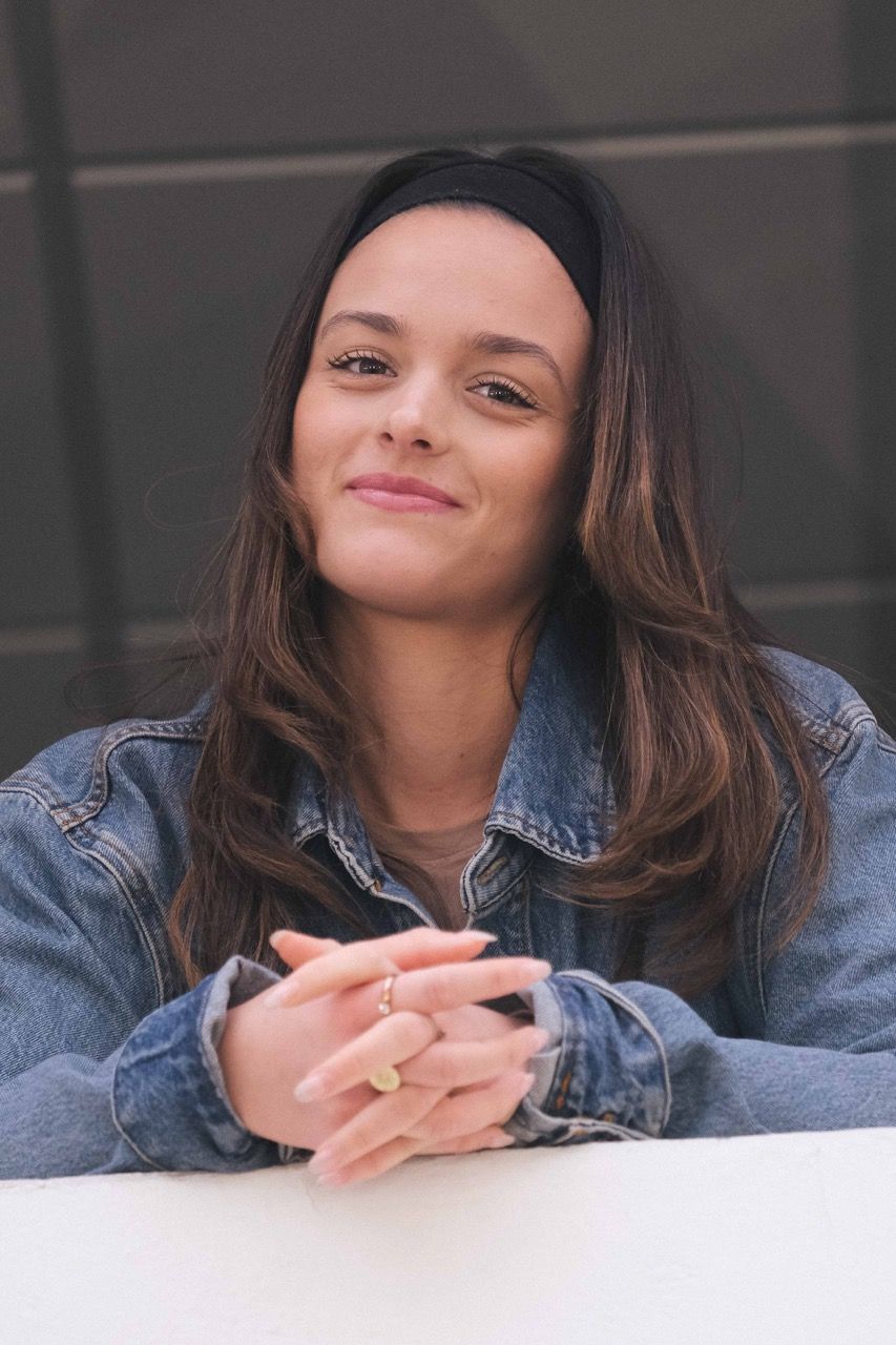 Étudiante souriante se tenant près d'une fenêtre, prise en portrait vertical